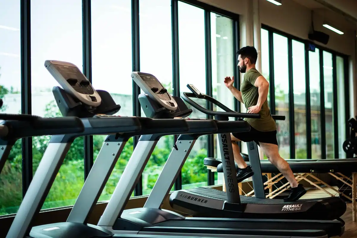 Bărbat care aleargă pe bandă într-o sală de fitness cu ferestre mari