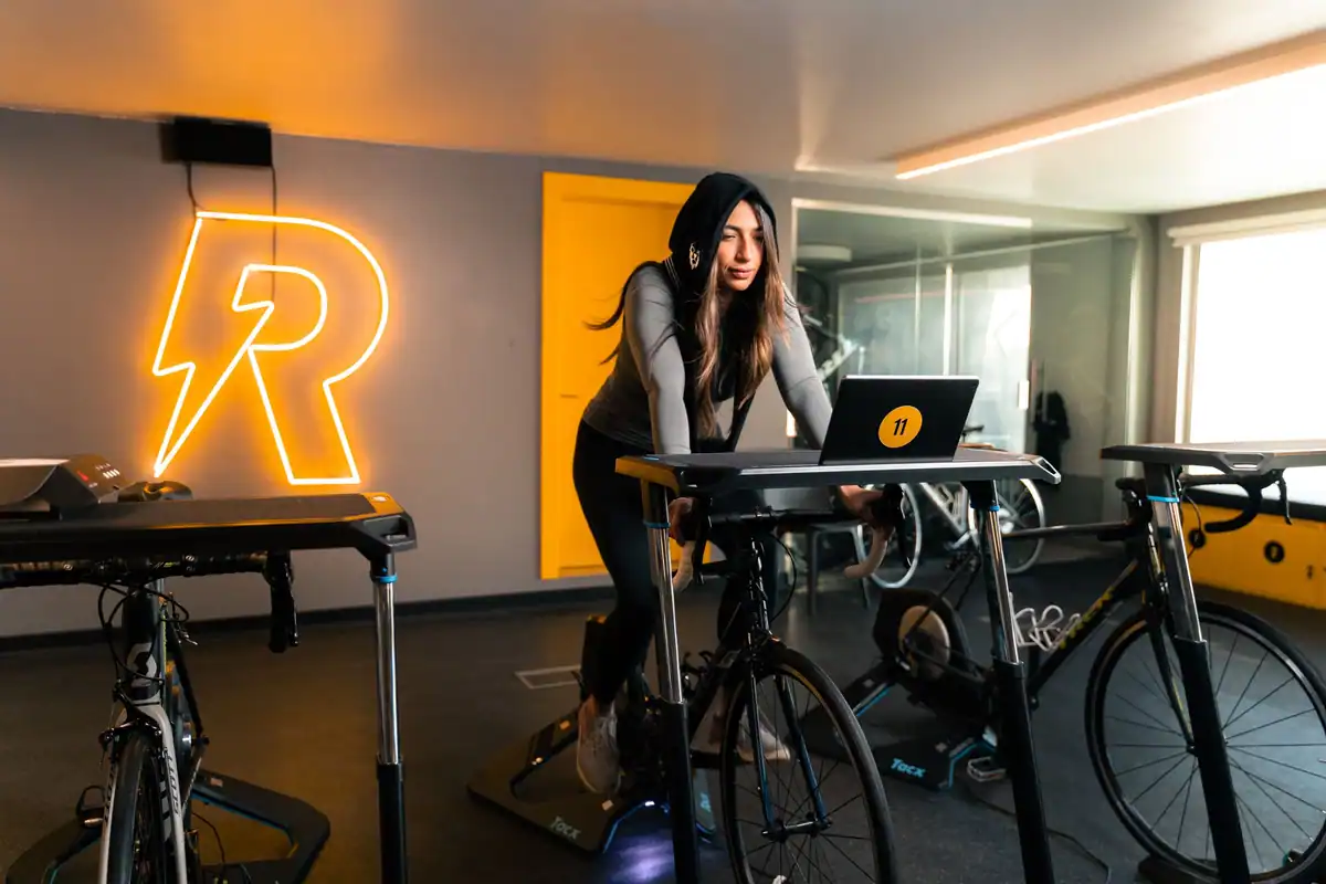 Femeie în echipament sportiv care pedalează pe o bicicletă staționară într-o sală de fitness