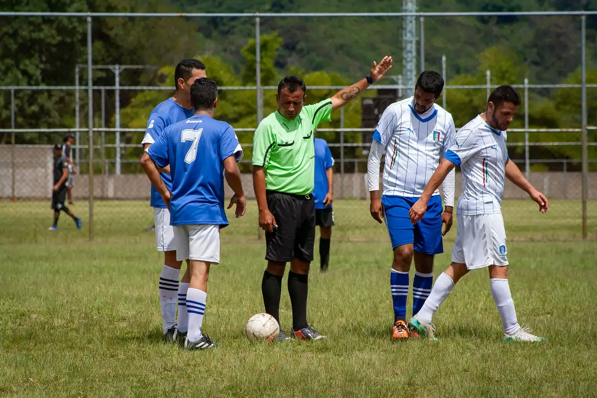 Arbitru de fotbal care arată cu brațul direcția unei lovituri, între jucători