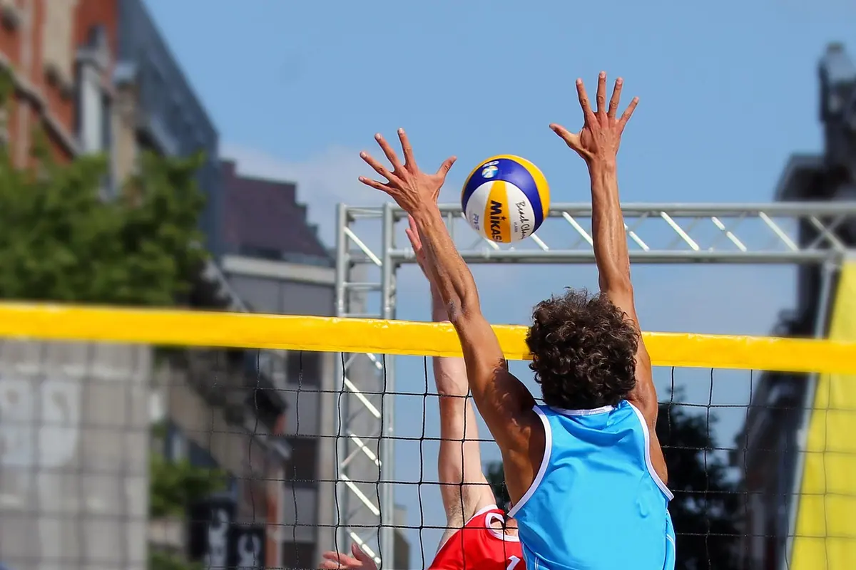 Jucător de volei care blochează mingea la fileu, cu brațele ridicate