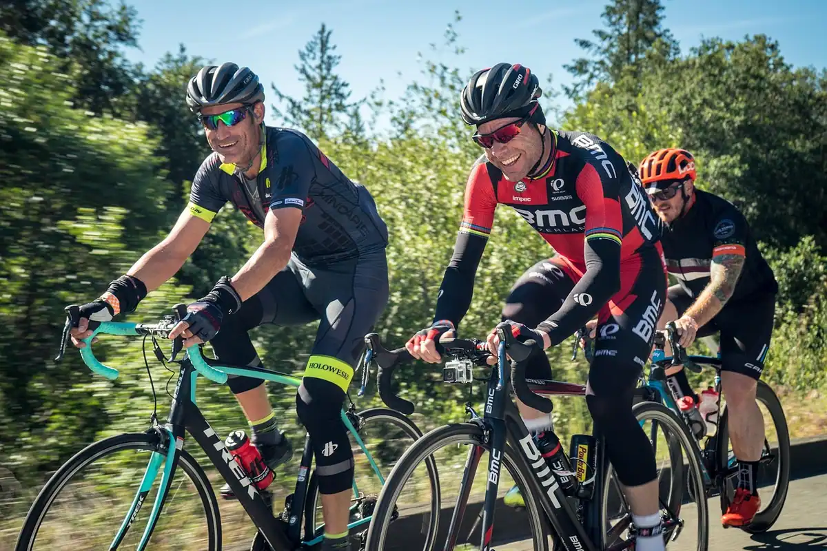 Grup de cicliști cu căști pe un drum, pedalând unul în spatele altuia într-o ieșire în grup