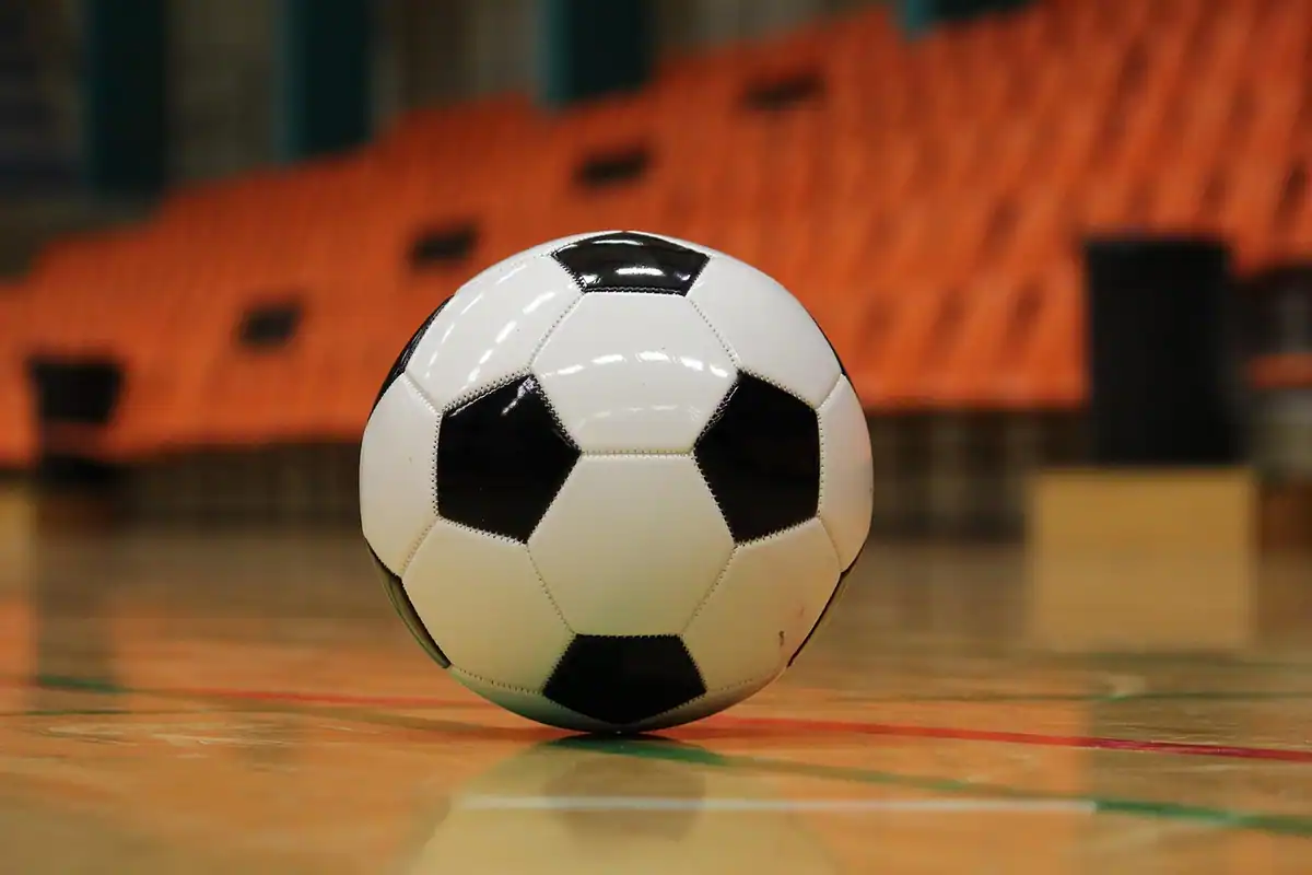Minge de futsal pe parchetul de lemn al unei săli, cu terenul interior în fundal