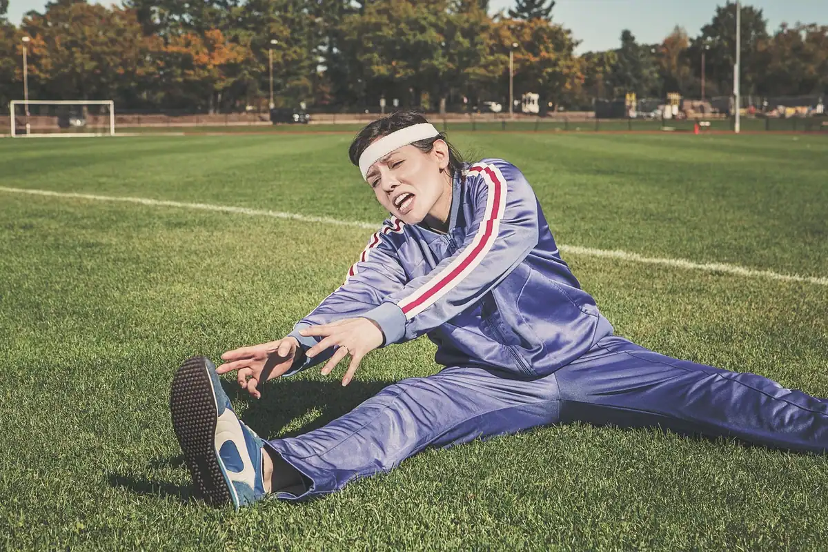 Sportivă care face exerciții de întindere pe iarbă, pentru încălzire sau recuperare