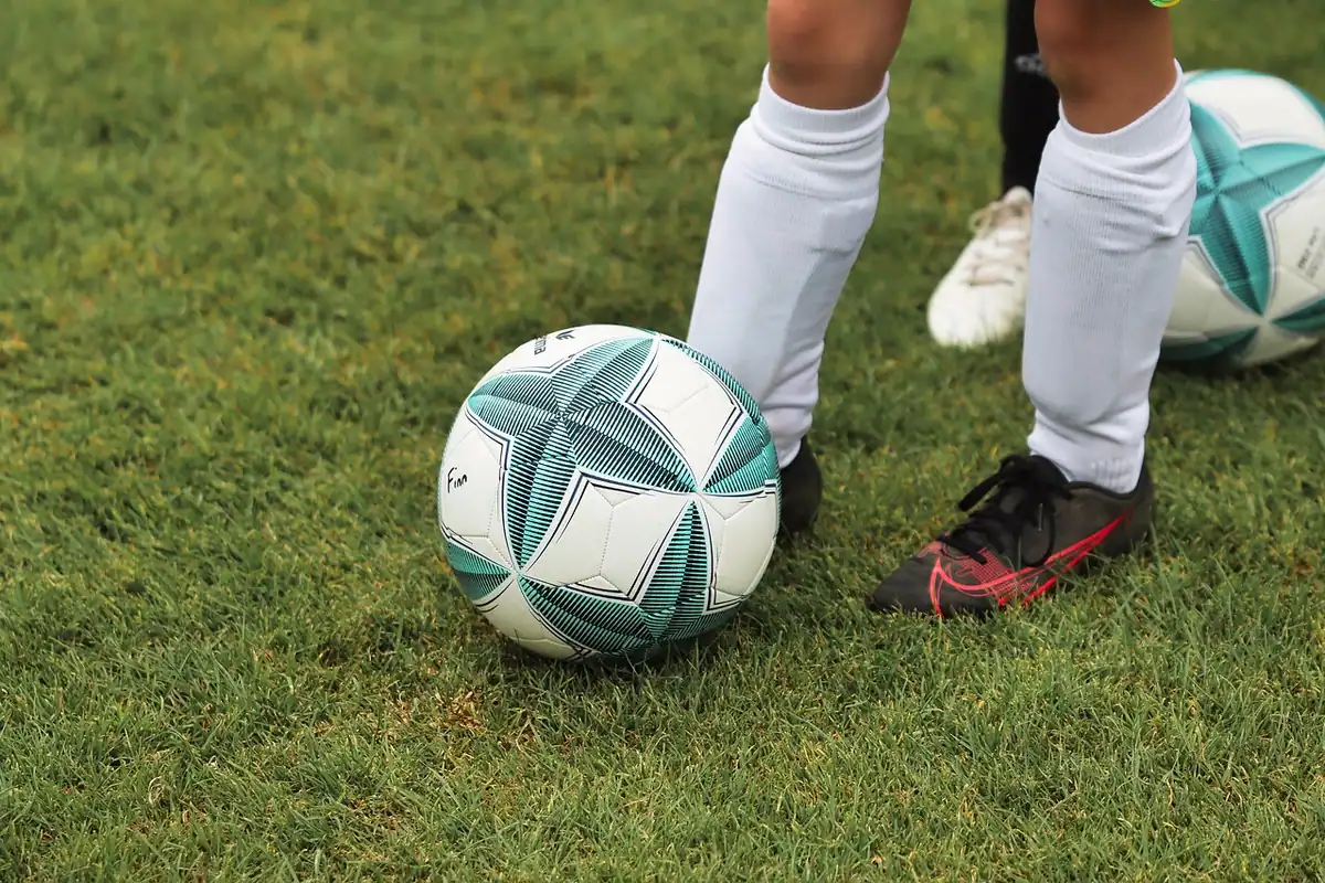 Ghete de fotbal cu crampoane lângă o minge, pe un teren cu iarbă naturală
