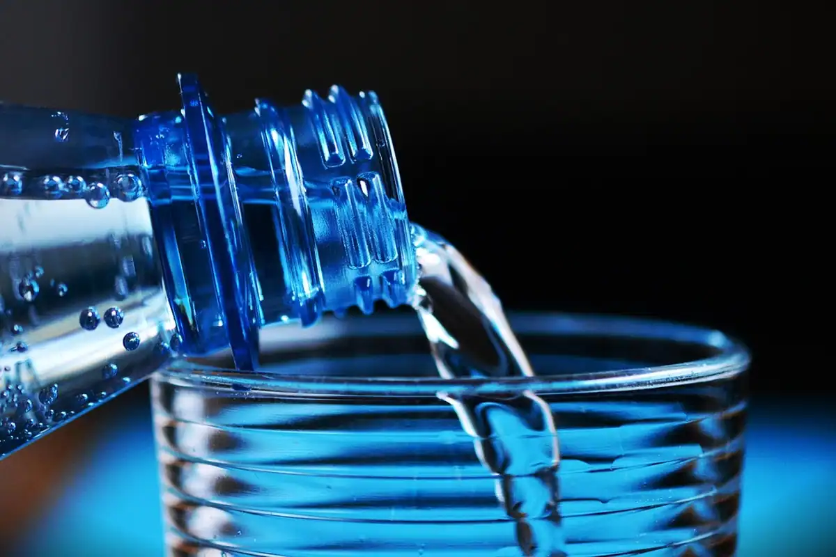 Apă turnată dintr-o sticlă de plastic într-un pahar transparent