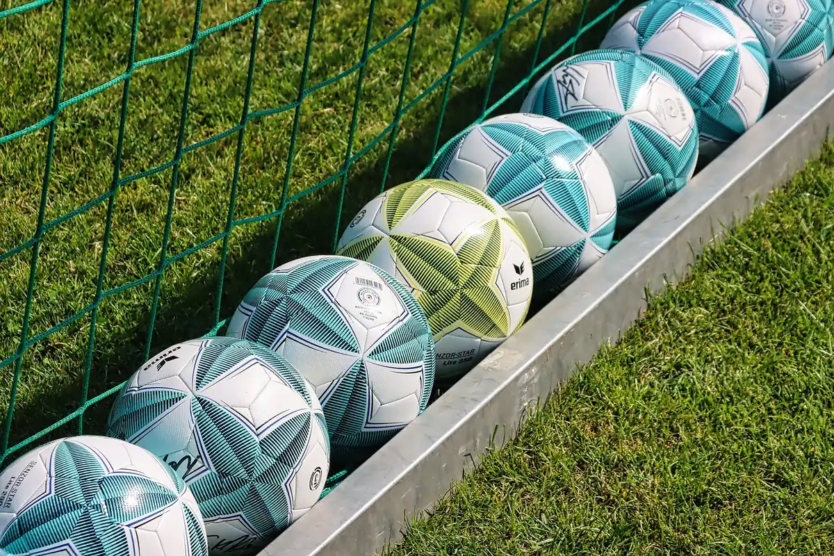 Mingi de fotbal aliniate lângă terenul de antrenament, în spatele unui gard