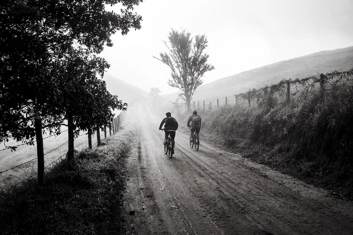 Doi bicicliști pe un drum de țară cu ceață, în fotografie alb-negru
