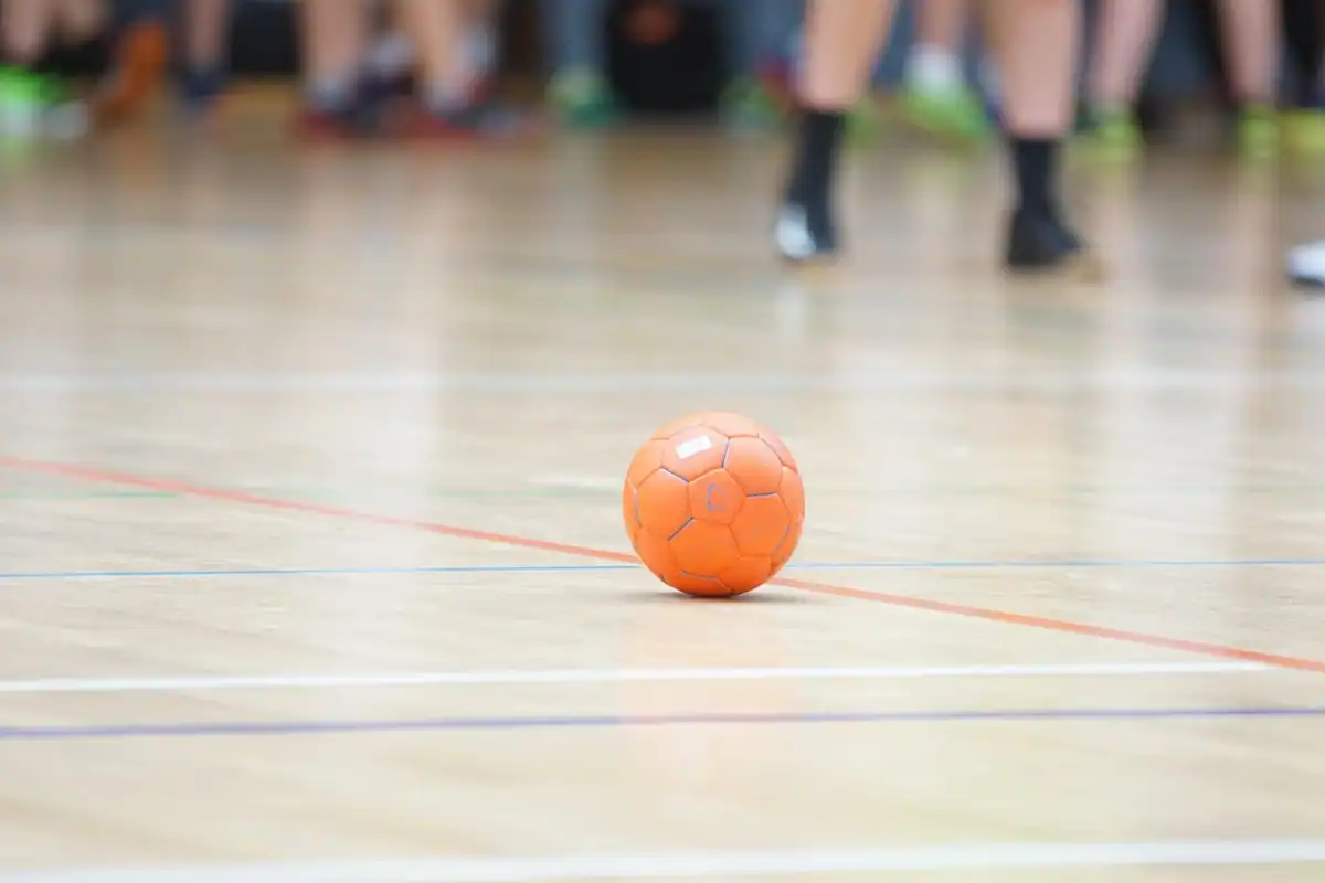 Podea de sală de sport cu linii colorate și o minge de handbal portocalie pe teren