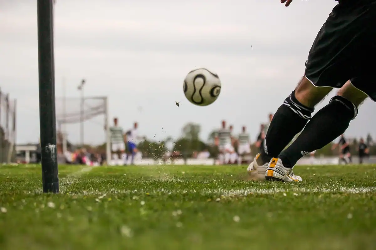 Jucător de fotbal care lovește mingea spre poartă pe un teren cu iarbă