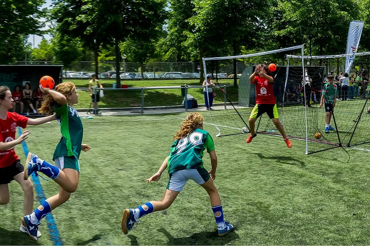 Copii care joacă handbal pe un teren cu gazon, cu porți mici în fundal