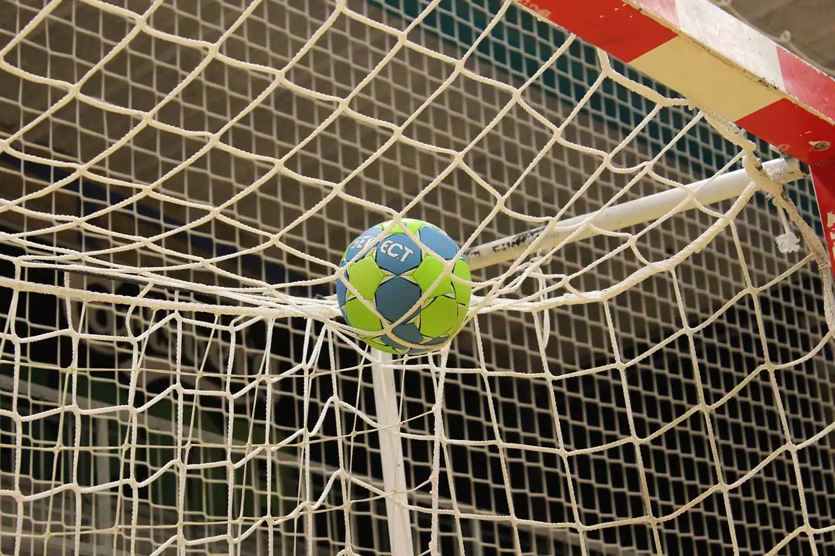 Minge de handbal prinsă în plasa porții, lângă bara laterală