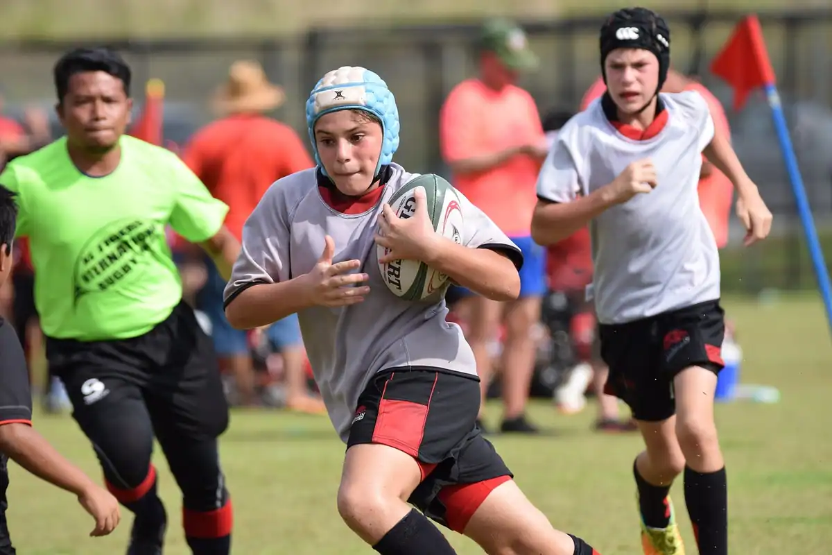Tânăr jucător de rugby care aleargă cu mingea, urmărit de adversari