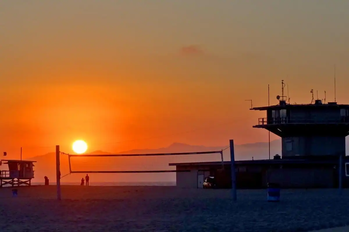 Fileu de volei pe plajă la apus, cu soarele coborând spre mare