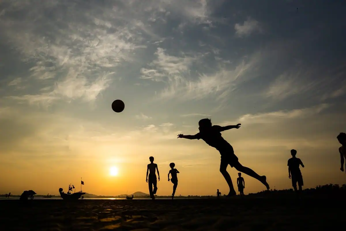 Siluete de copii care joacă fotbal pe un teren deschis, la apus