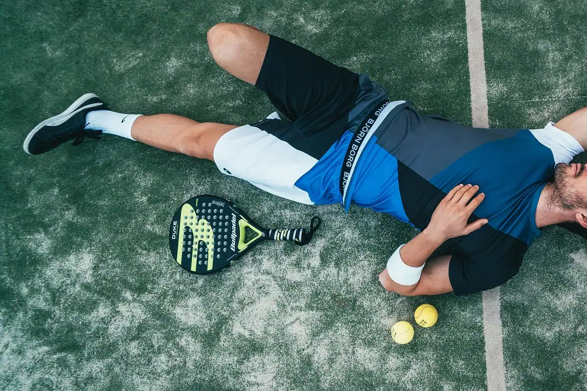 Sportiv epuizat întins pe teren, cu racheta lângă el, după un efort prelungit