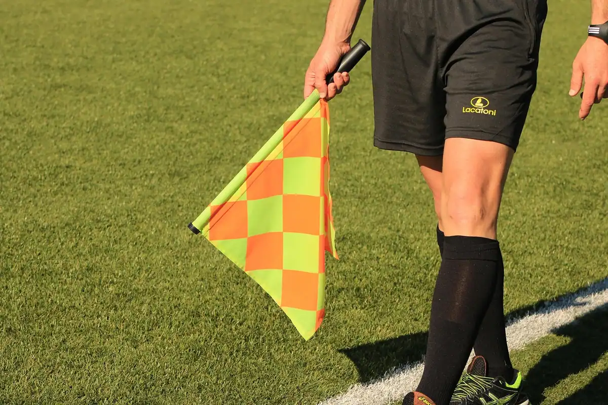 Arbitru asistent cu fanionul ridicat pe marginea terenului de fotbal